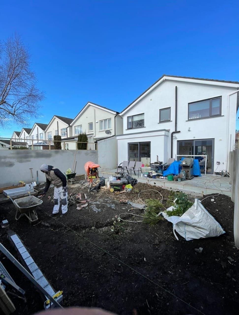 Rear garden mid-build, with bare soil, materials and a worker preparing the ground